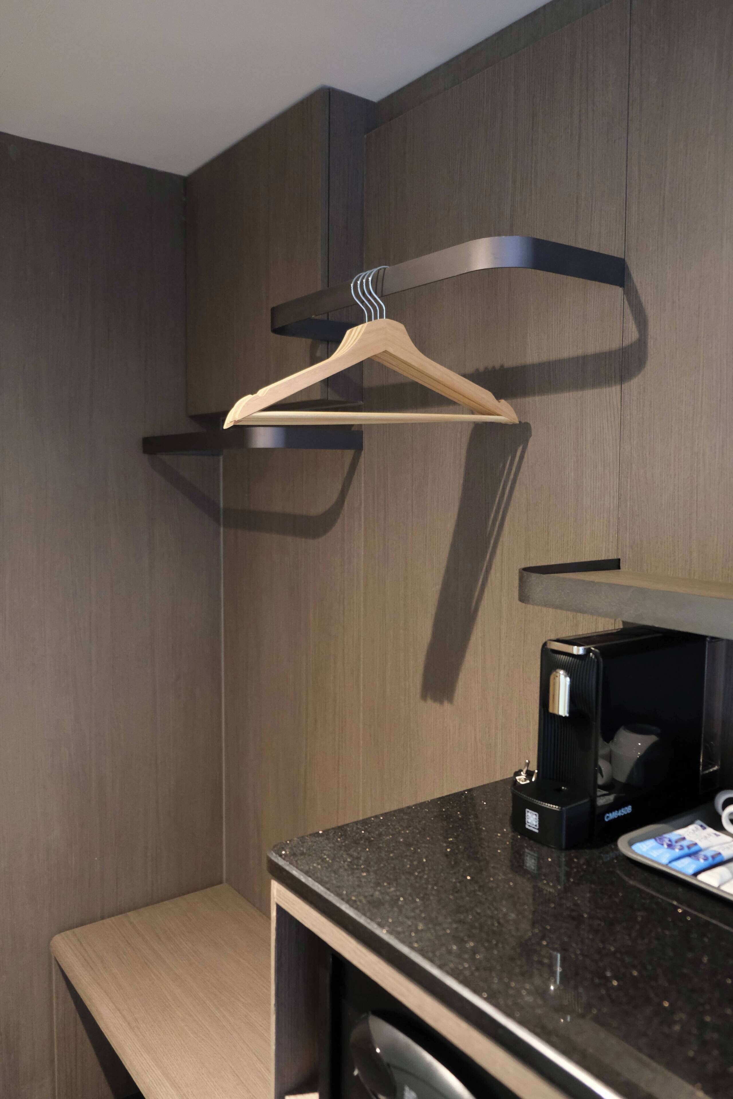 A modern bathroom with a wooden bench, a black countertop, and a coffee maker.