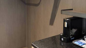 A modern bathroom with a wooden bench, a black countertop, and a coffee maker.