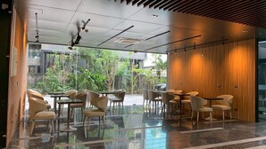 A modern indoor space with a glass wall, wooden paneling, and a variety of seating arrangements including tables and chairs.