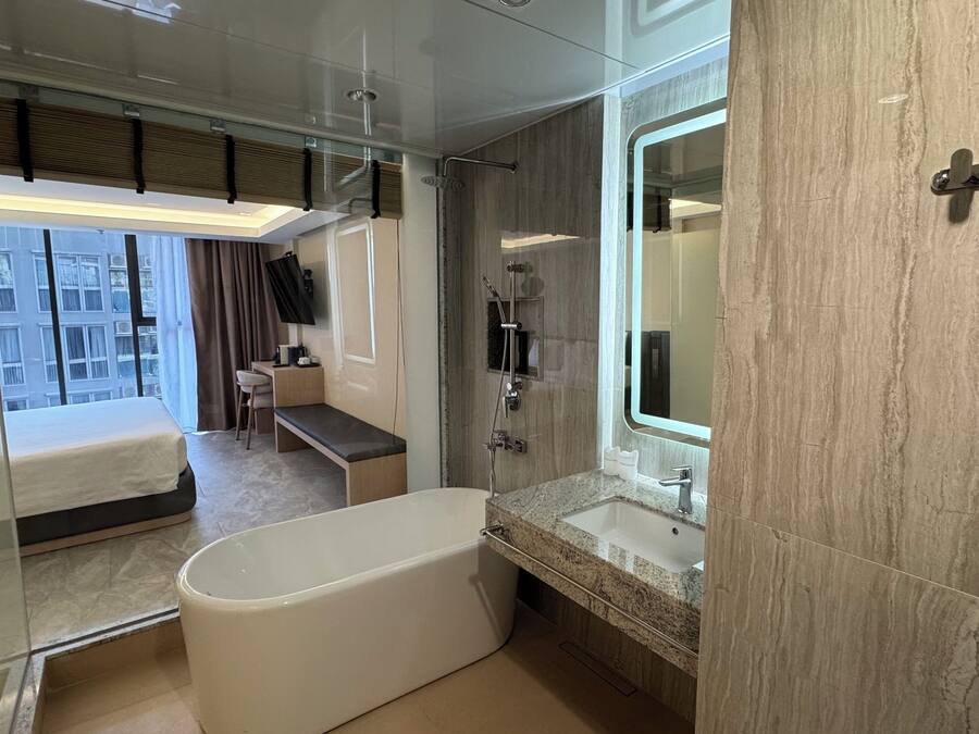 Een moderne hotelkamer met een groot bad, een wastafel met spiegel, een douche en een bureau met stoel, plus een bed.