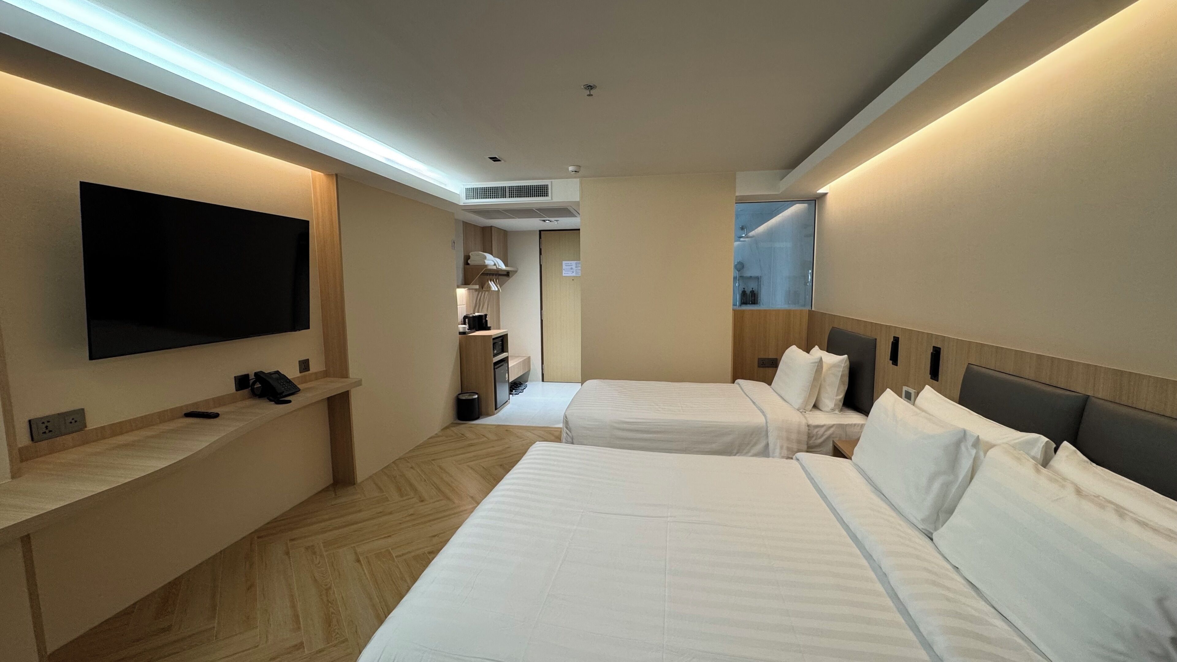 A hotel room with two beds, a TV, a desk with a phone, and a bathroom visible through an open door.