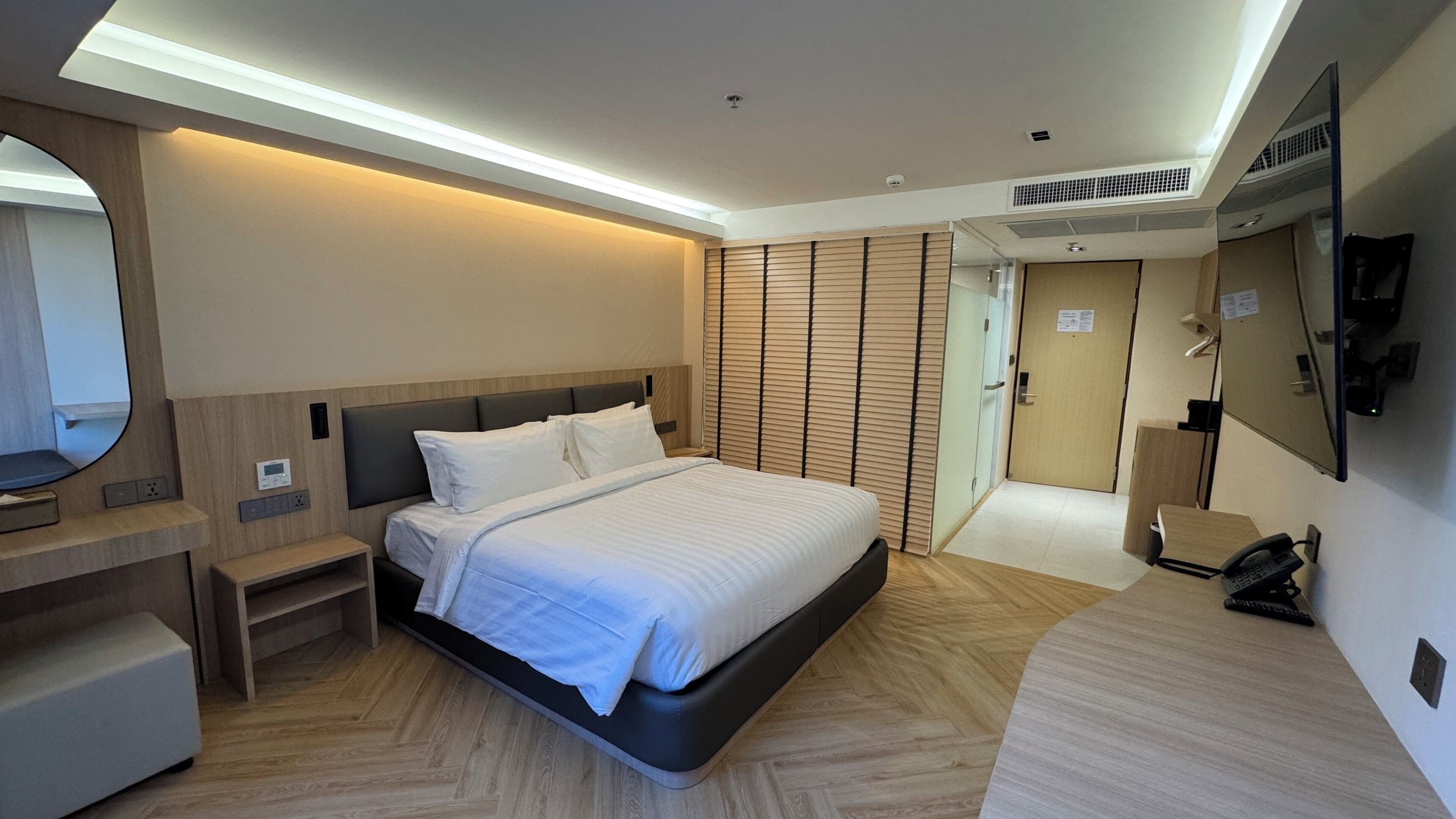 Una habitación de hotel moderna con cama, mesita de noche, espejo y escritorio con teléfono.