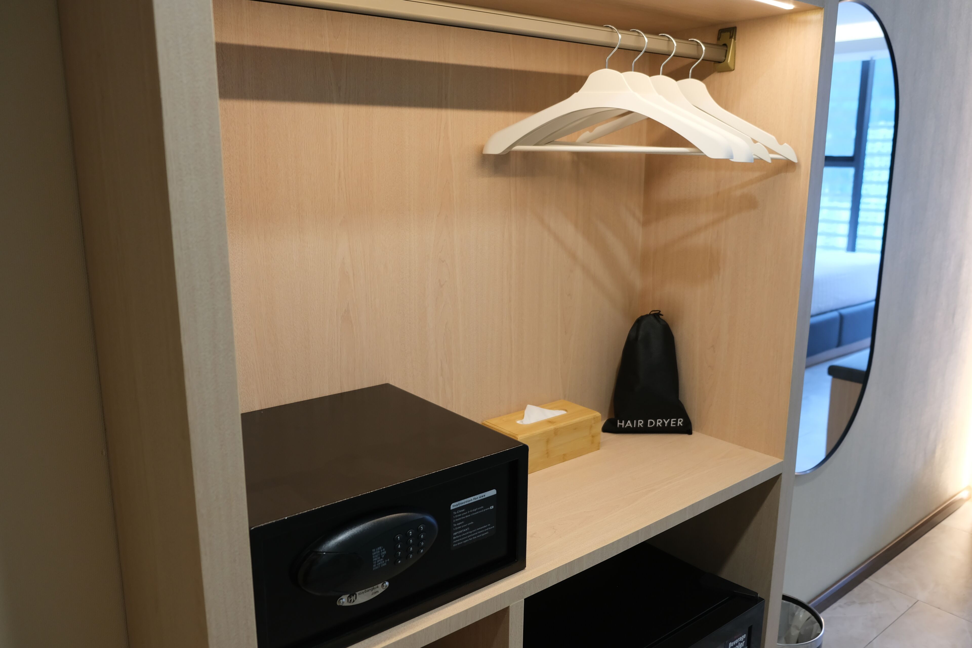 Hotelkamer met een houten garderobe, een haardroger, een doos en een zwart elektronisch apparaat op de plank.