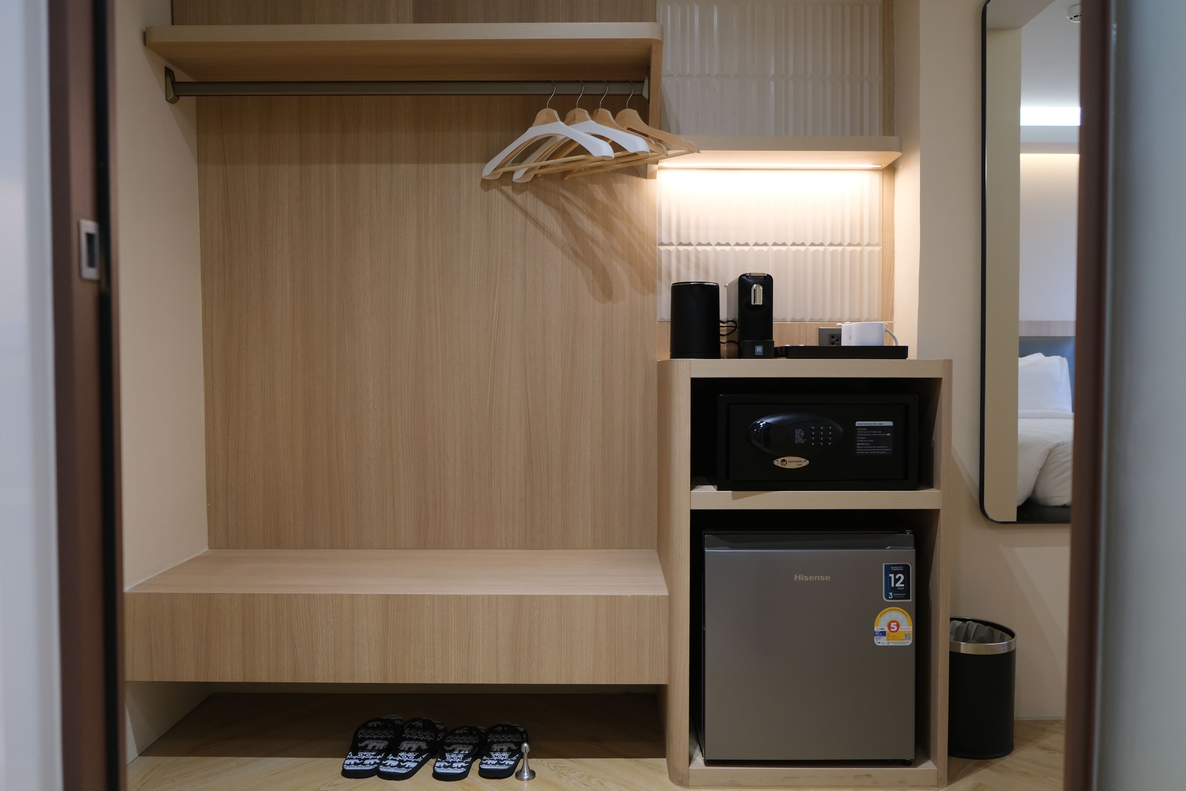 A compact hotel room with a wooden wardrobe, a small refrigerator, a microwave, and a shoe rack.