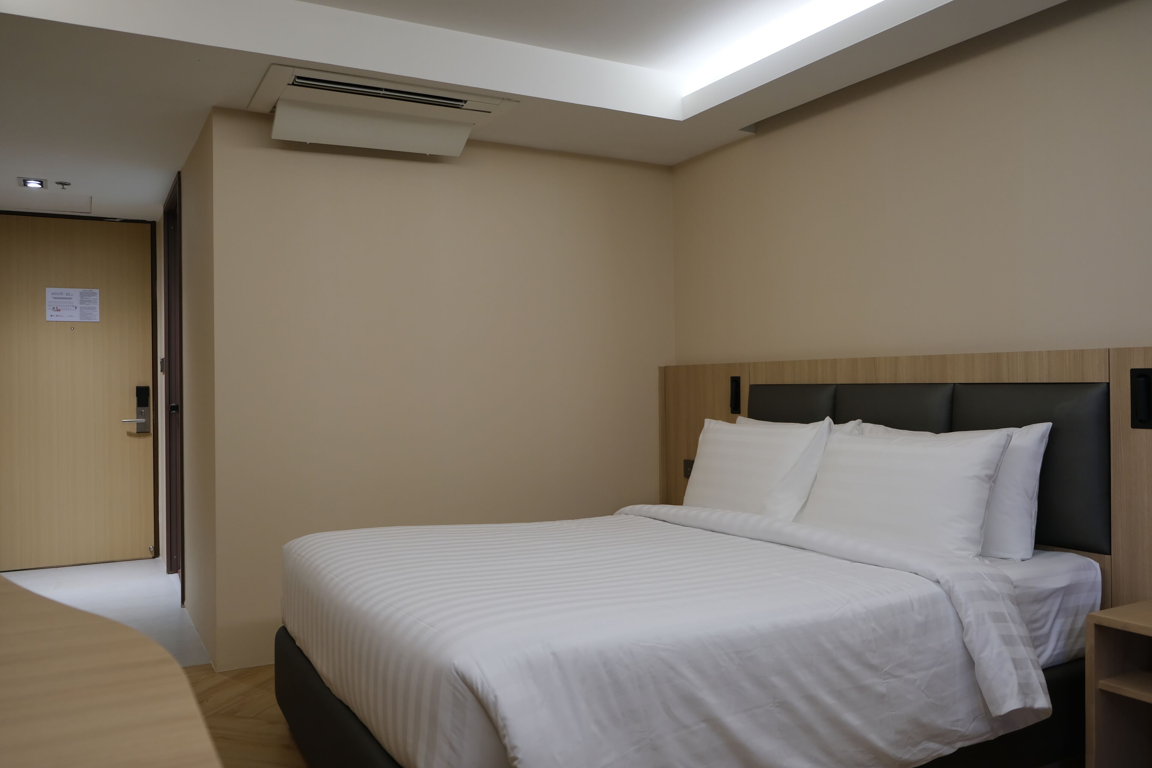 A hotel room with a bed, a wooden headboard, a bedside table, and a door.
