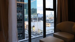 A hotel room with a large window offering a view of a cityscape, including modern buildings and a clock tower.