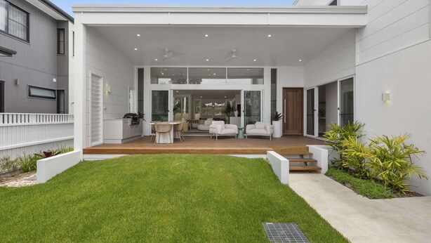 Ein modernes Haus mit geräumiger Terrasse, einem Essbereich und einer durch große Glaswände einsehbarer Küche.