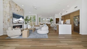Ein modernes Wohnzimmer mit Steinwand, Kamin und großem Fernseher. Es gibt eine Küchenzeile mit Holzausstattung und einem Edelstahlkühlschrank.