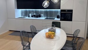 Een moderne keuken met een centraal eiland, een ingebouwde oven en een eethoek met een glazen tafel en stoelen.