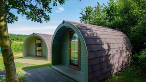 Deux petites cabanes aux lignes courbes, dotées de terrasses en bois et entourées de verdure.