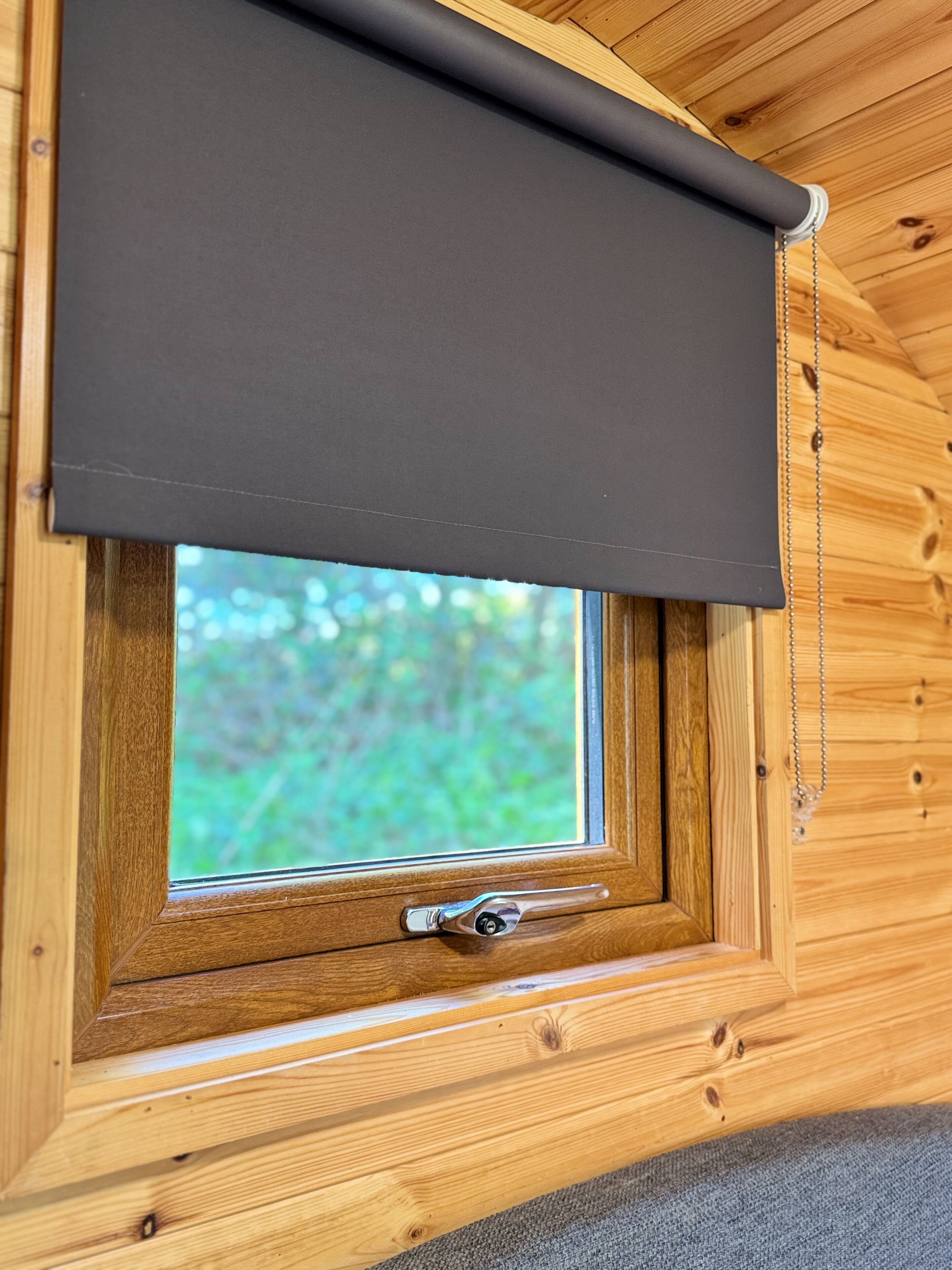 A window with a dark roller blind, wooden frame, and a metal handle.
