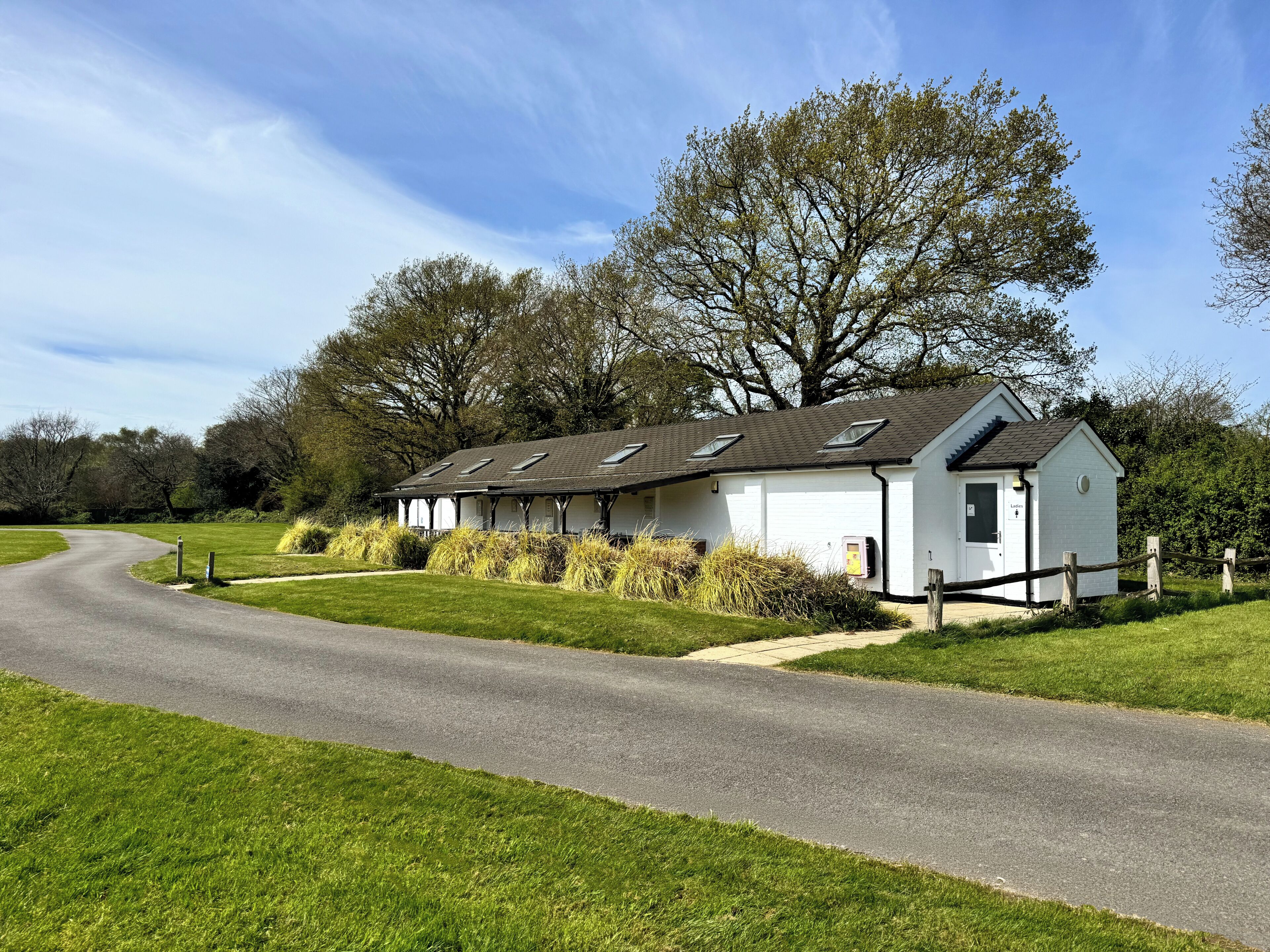 A white building with multiple windows and a sloped roof, surrounded by a grassy area and trees.