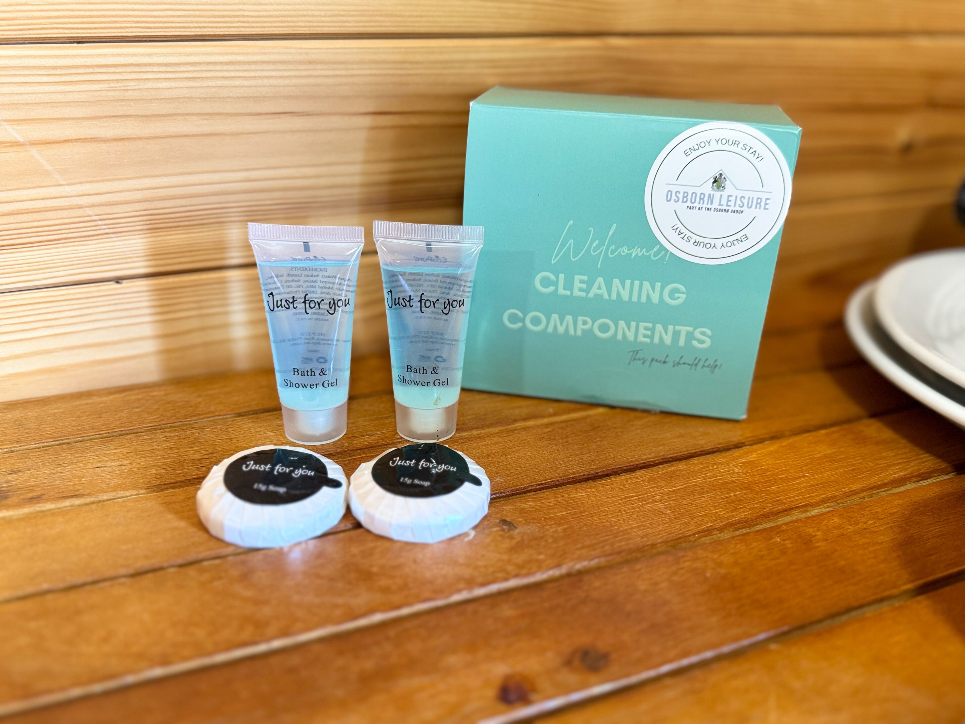A wooden surface with a teal box labeled 'OSBORN LEISURE CLEANING COMPONENTS' and two transparent tubes with 'Just for you' labels.