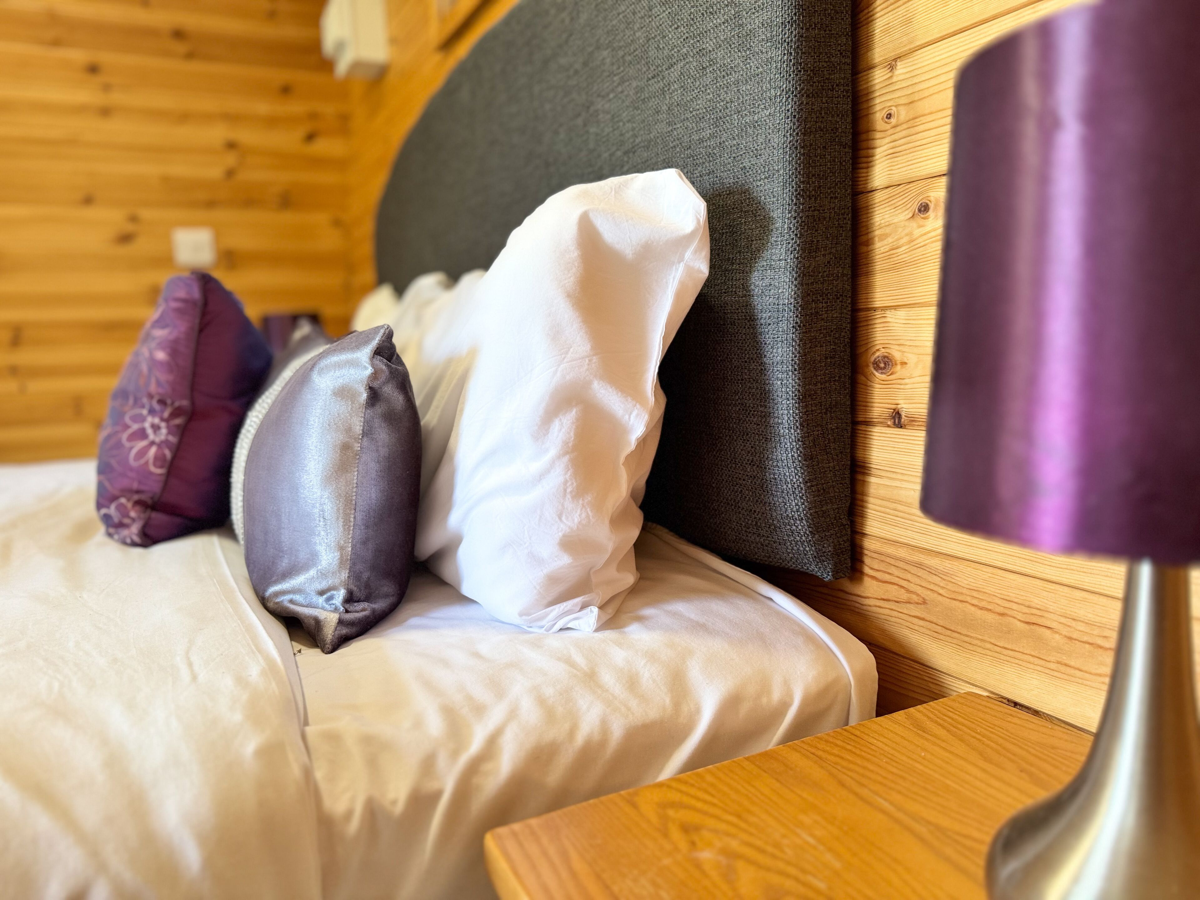 A wooden cabin interior with a bed, pillows, and a lamp.