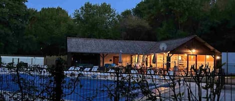 A poolside building with a tiled roof, surrounded by a fence and trees.