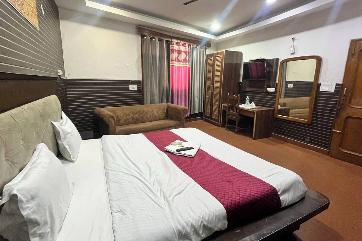 A hotel room with a large bed, a sofa, a desk, a TV, and a wardrobe.
