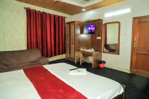 Habitación de hotel con cama, escritorio, silla, televisor, espejo y armario.