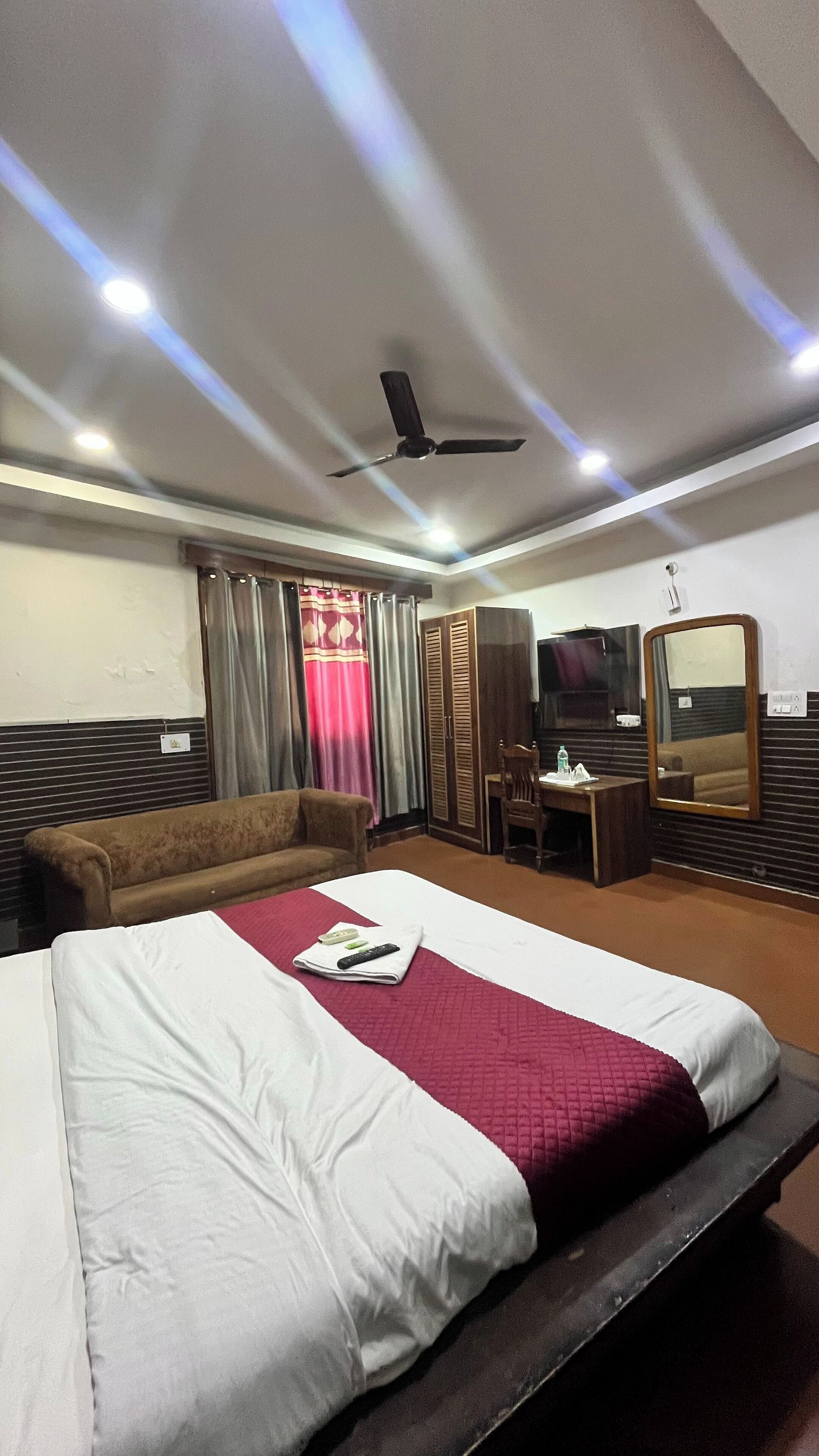 Habitación de hotel con cama, sofá, escritorio con silla, armario y ventilador de techo.