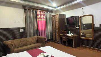 Habitación de hotel con cama, sofá, escritorio con silla, armario y ventilador de techo.