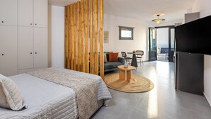 Una habitación de hotel moderna con una cama grande, un separador de madera, un sofá, una mesa de comedor y un televisor.