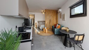 Un espacio habitable compacto con kitchenette, una zona de comedor con una mesa redonda y sillas, un sofá y un ventanal grande.