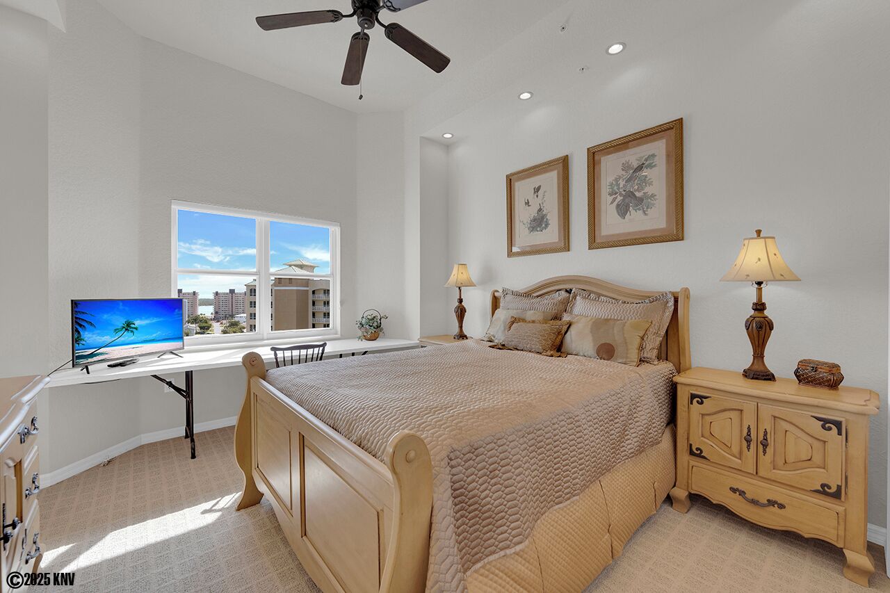 A bedroom with a bed, desk, and computer, a window with a view, and two framed pictures on the wall.
