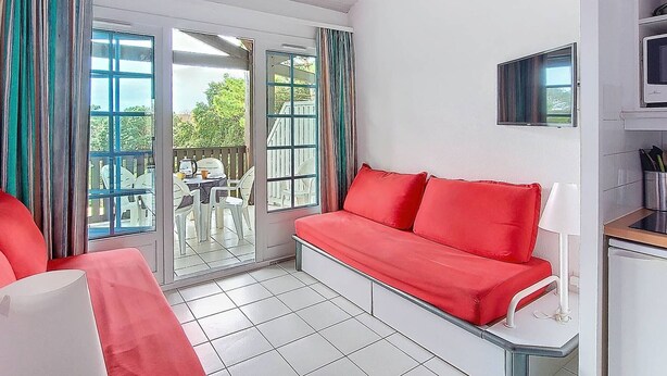 Une pièce avec un canapé rouge, un téléviseur et un coin repas comprenant des chaises et une table.