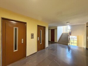 Ein Korridor mit zwei Holztüren, einem Lichtschalter und einer Treppe, die zu einer oberen Etage führt.