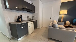 A compact kitchen with dark cabinets, a white dishwasher, and a grey sofa in a living area with a lamp and a vase. - Two-room apartment in Sète - Terrace, Parking, WiFi (Sète)