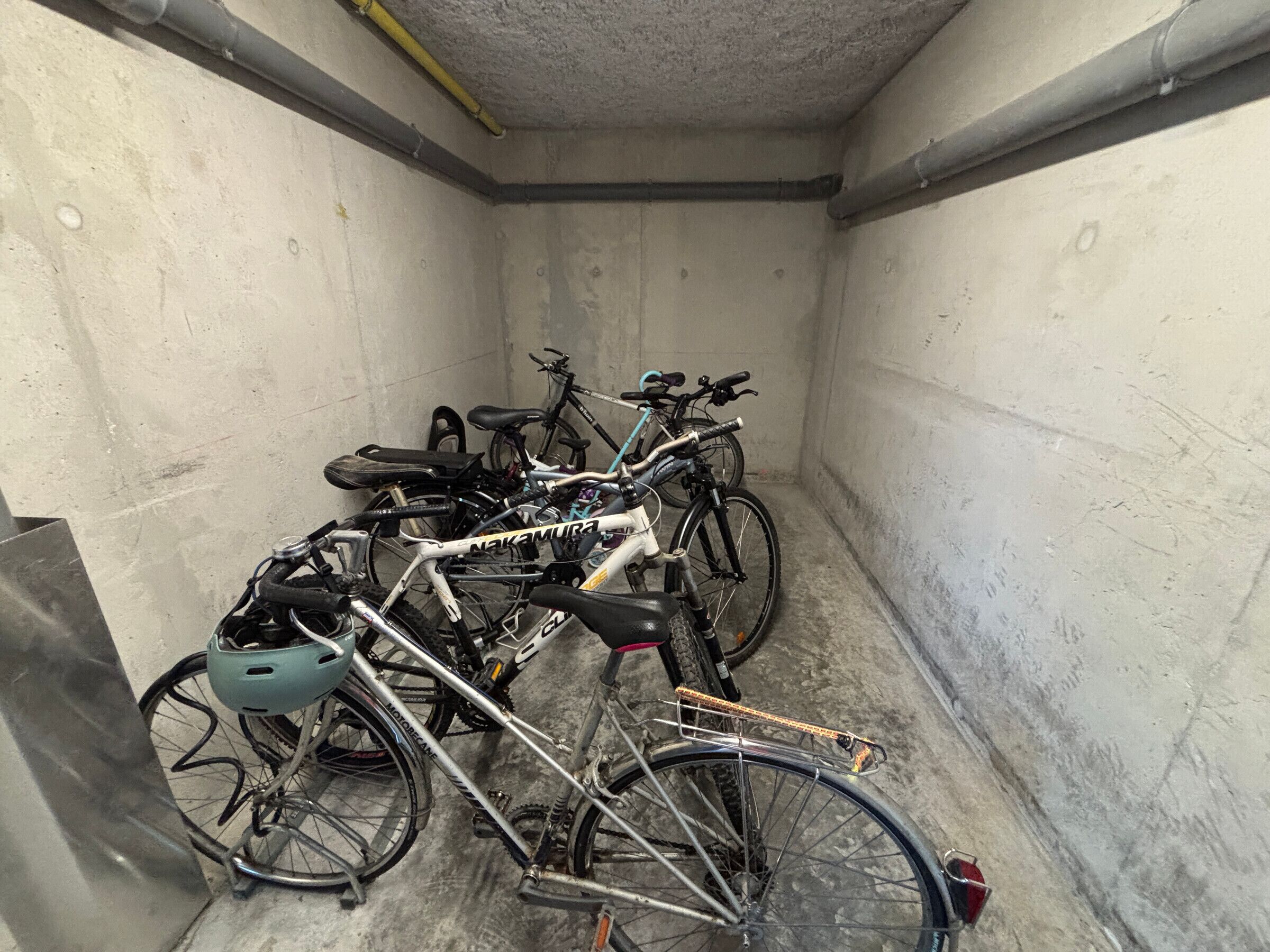 A narrow, concrete-walled parking area with bicycles parked against the walls.