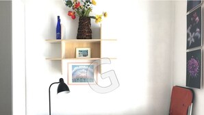 A bedroom with a bed, a desk with a lamp, a shelf with pictures and a vase with flowers. - Cozy studio downtown near the beach (La Tranche-sur-Mer)
