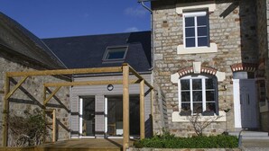 A stone building with a wooden pergola entrance, a visible door, and a window with a white frame.