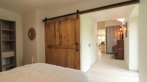 A bedroom with a large bed, a wooden wardrobe, and a sliding door leading to a hallway.