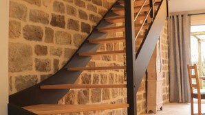 A staircase with wooden steps and black railings, leading to a room with a stone wall and a window with curtains.