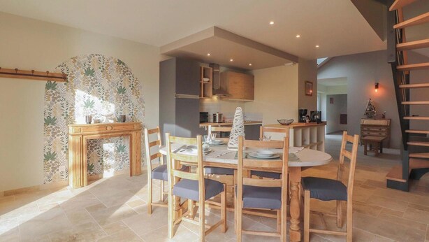 A dining area with a round table and chairs, a kitchen in the background, and a staircase to the right.