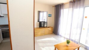 A compact living space with a kitchenette, a wooden table with a potted plant, and a sliding glass door with curtains. - Beautiful One-Bedroom Penthouse with Spectacular Terrace in Central Salou (Salou)