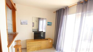 A room with a wooden dresser, a television, and a window with curtains. - Beautiful One-Bedroom Penthouse with Spectacular Terrace in Central Salou (Salou)