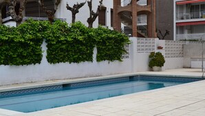 A swimming pool with a tiled deck, surrounded by a white wall with green ivy and a small potted plant. - Beautiful One-Bedroom Penthouse with Spectacular Terrace in Central Salou (Salou)