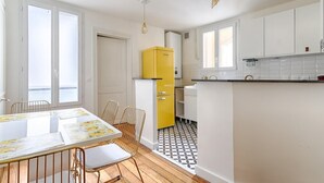 Eine moderne Küche mit weißen Schränken, einem gelben Kühlschrank und einem Essbereich mit Tisch und Stühlen.