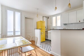 Eine moderne Küche mit weißen Schränken, einem gelben Kühlschrank und einem Essbereich mit Tisch und Stühlen.