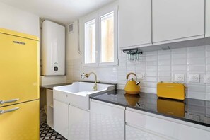 A kitchen with a yellow refrigerator, white cabinets, a sink with a gold faucet, and a yellow kettle on the countertop. - Central Paris – Mid-Term Fully Equiped (Paris)