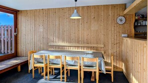 Una stanza con rivestimenti in legno, un tavolo da pranzo con sedie, un lampadario, una sveglia e una panca di legno vicino a una finestra.