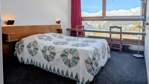 Camera d'albergo con un letto, una scrivania, una sedia, una finestra vista montagna e una lampada.