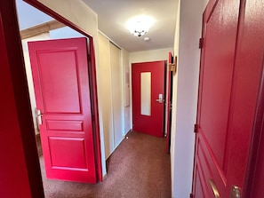A hallway with red doors, carpeted floor, and a ceiling light fixture. - Apartment for 4, ski-in/ski-out with balcony, parking included (Lanslebourg-Mont-Cenis)