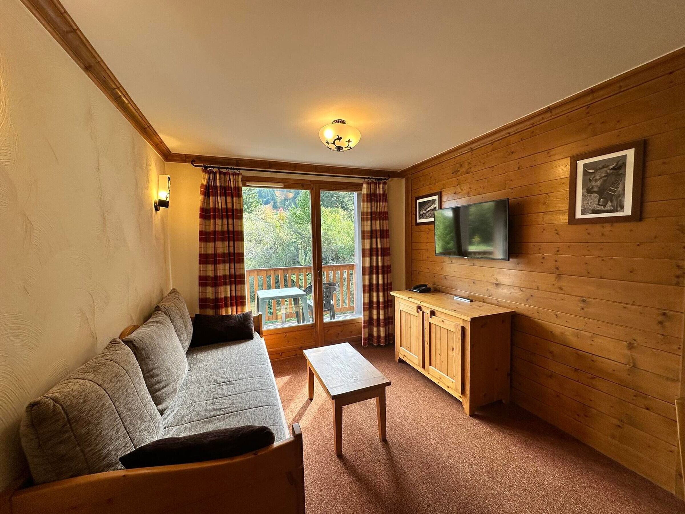 A cozy room with a sofa, a small table, a wooden cabinet, and a TV mounted on the wall.