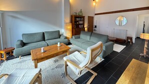 A cozy living room with a grey sofa, a wooden coffee table, and a white armchair. There is a bookshelf and a mirror on the wall. - Spacious apartment for 8, close to slopes in Serre Chevalier (La Salle-les-Alpes)