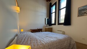 A bedroom with a bed, a bedside table, a lamp, a dresser, a mirror, and a window with curtains. - Spacious apartment for 8, close to slopes in Serre Chevalier (La Salle-les-Alpes)