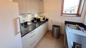 A compact kitchen with white cabinets, a black countertop, a coffee maker, a microwave, and a window with a view of buildings. - Spacious apartment for 8, close to slopes in Serre Chevalier (La Salle-les-Alpes)