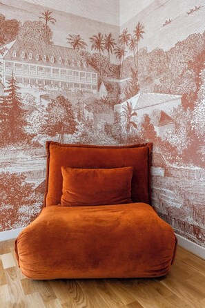 Ein Bett mit einer strukturierten, orangefarbenen Bettdecke vor einer Wand mit einem detaillierten Wandgemälde einer tropischen Landschaft.