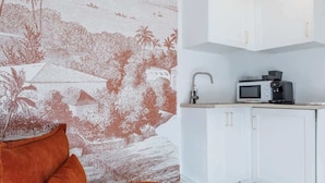 A modern kitchen with white cabinetry and a microwave, a wooden floor, and a vibrant orange sofa with a cushion. - Near Paris - 25 minutes from Eiffel Tower (Issy-les-Moulineaux)